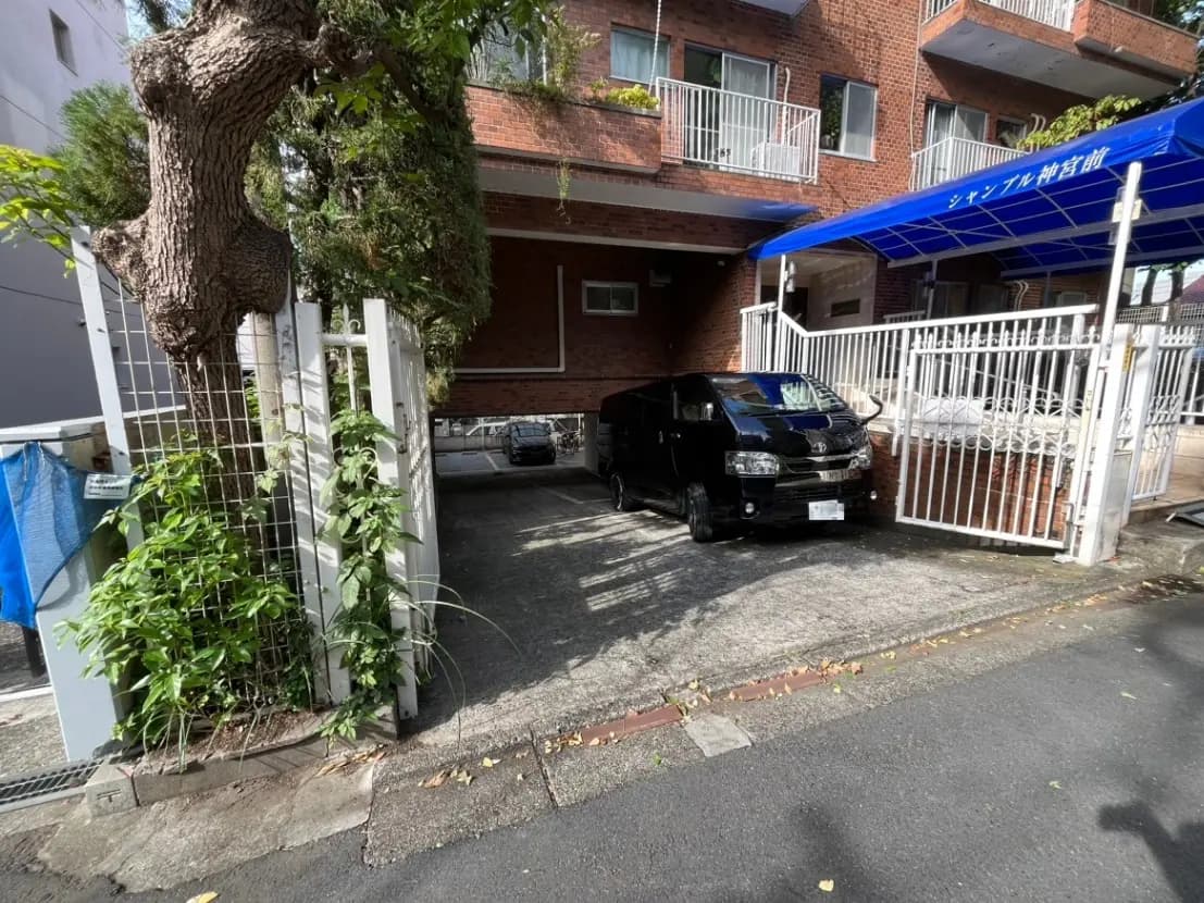 日本の住宅街にあるレンガ造りのアパートメント、門と植栽、駐車スペースに黒い車
