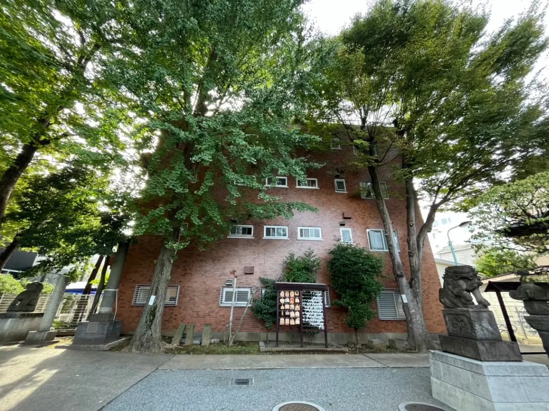 緑に囲まれたレンガ造りの建物と、前面に配置された彫刻がある公共のスペース