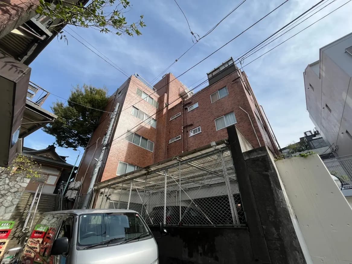 都市の住宅街にある赤レンガのアパート建物、周囲に植物と他の家々、晴れた日の景色