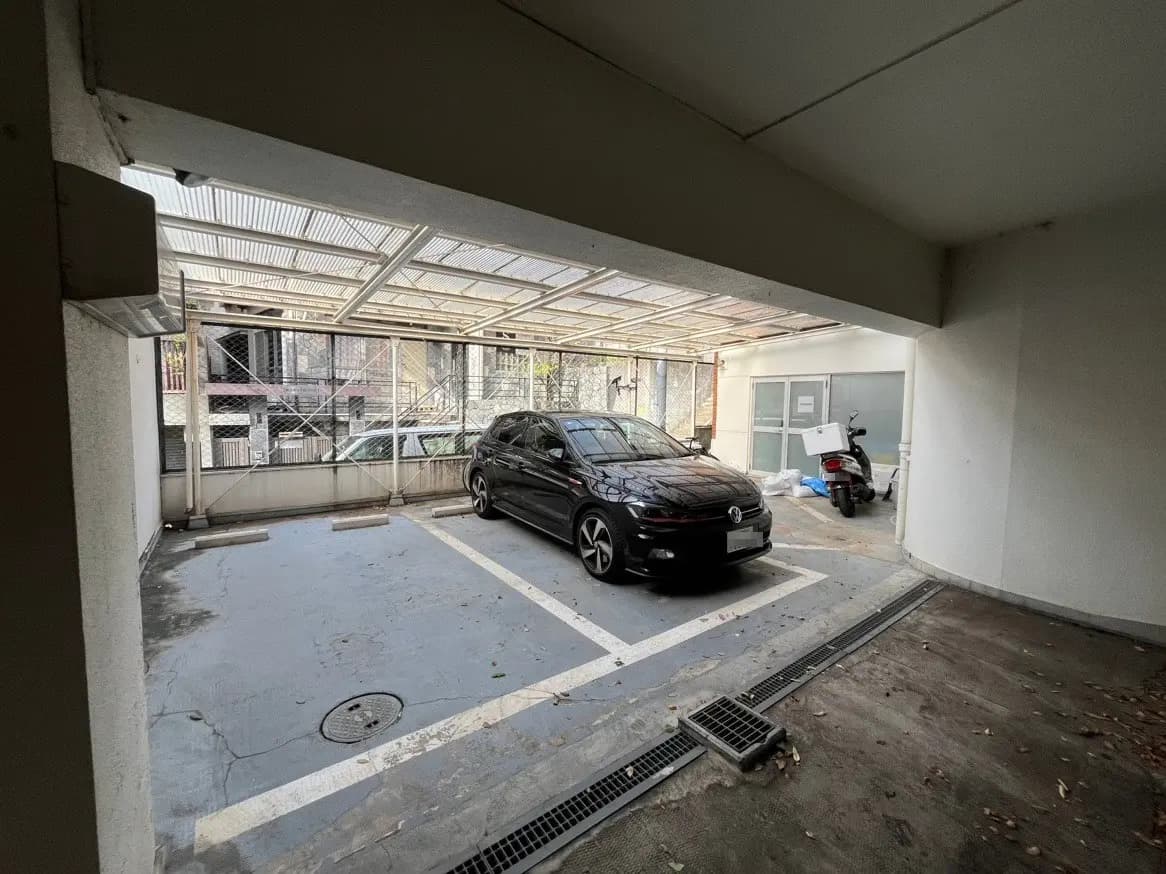屋根付きの駐車場に停められている黒色のセダン車とスクーター、コンクリートの床と透明な屋根