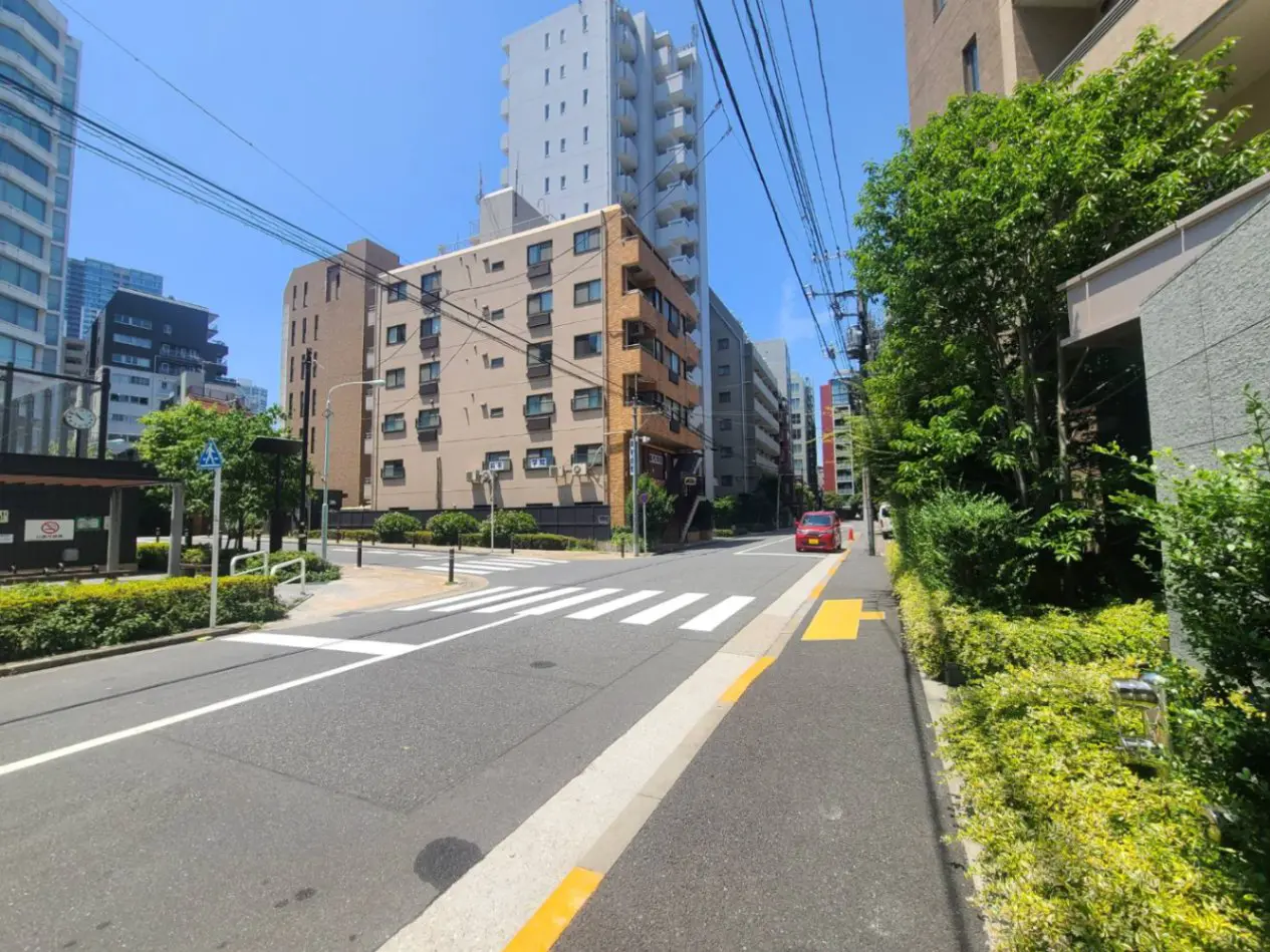 - 都市の通り、十字路、周囲にマンションや緑豊かな植栽、晴れ渡る青空が広がる風景