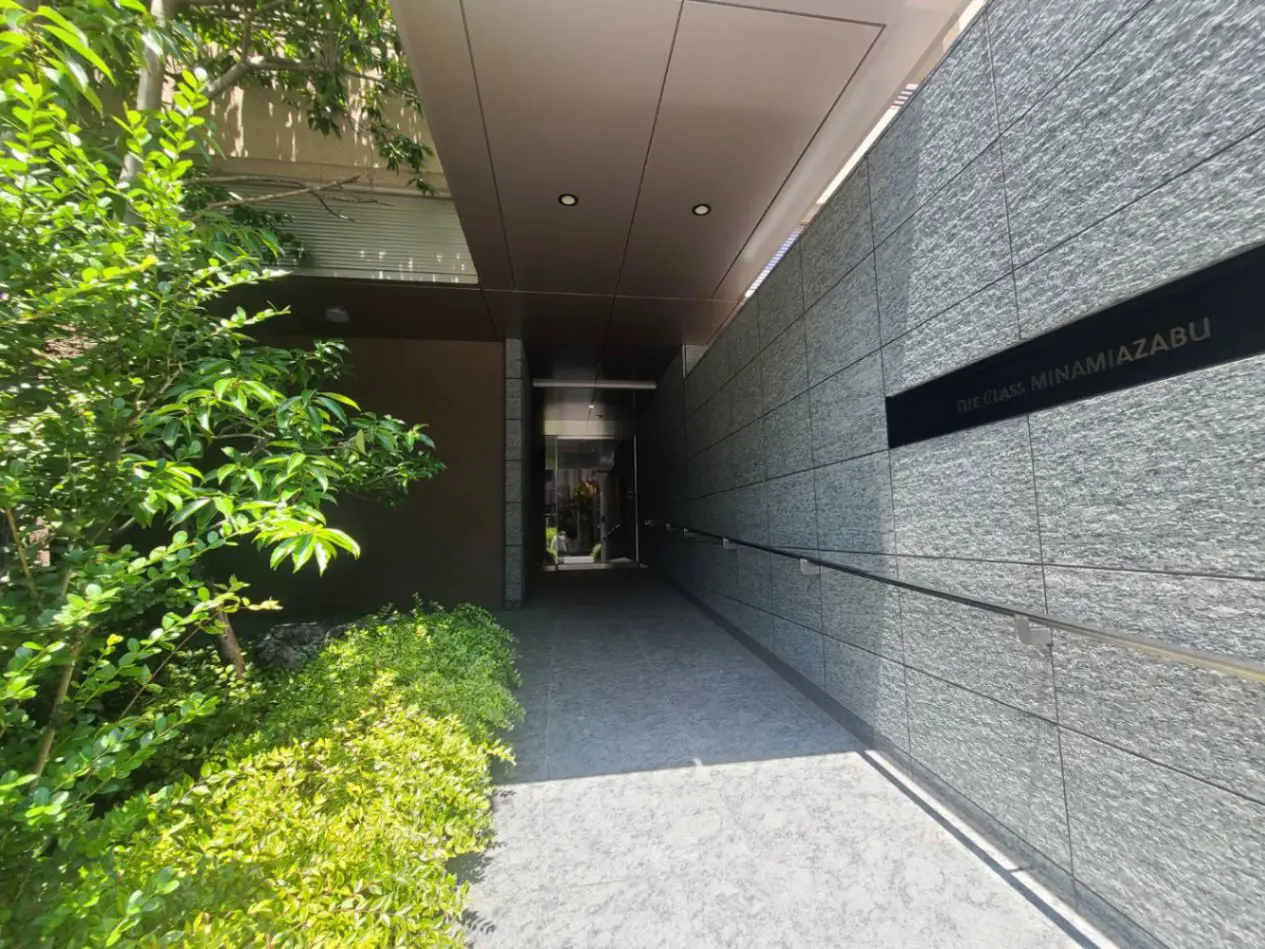 - モダンな建物のエントランス、緑豊かな植栽とスムーズなアクセスのための手すりがある歩道が特徴