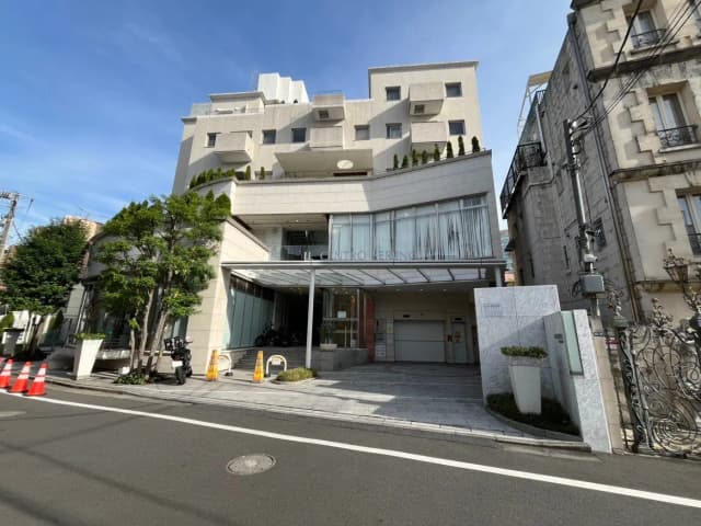 現代的な外観のマンションと入口、青空と緑の植物が映える都市の住宅風景