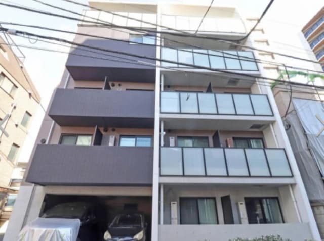 モダンな外観のアパートメントビル、バルコニーと窓が並ぶスタイリッシュなデザイン、駐車スペースには車が停まっている様子