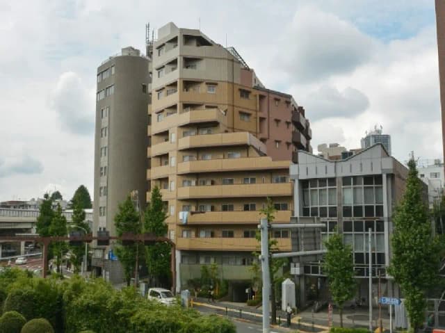 - 都市部に立つ複数の高層ビル、異なるデザインと色のファサード、周囲には緑の樹木が点在する風景