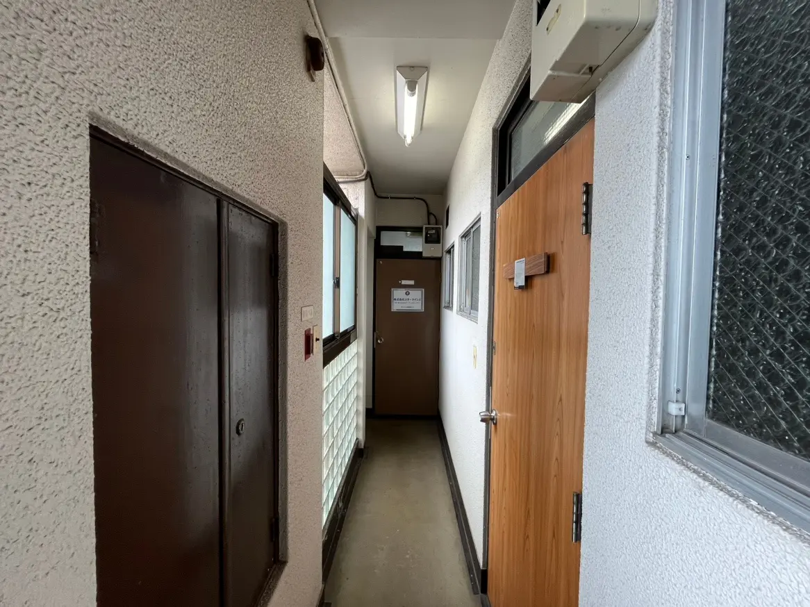 光が差し込む明るい廊下、左側に茶色の木製ドア、右側にガラス窓がついたオフィスやアパートメントの内部通路