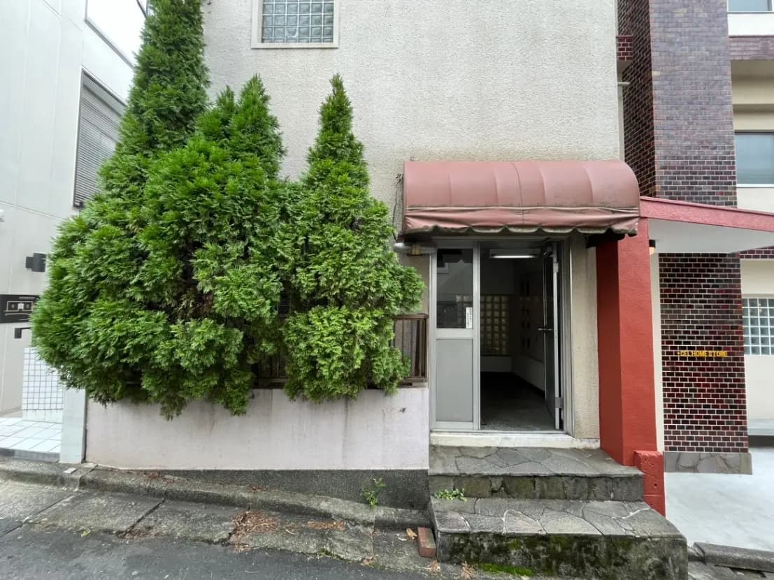 建物のエントランスと郵便受け、樹木が生い茂る外観