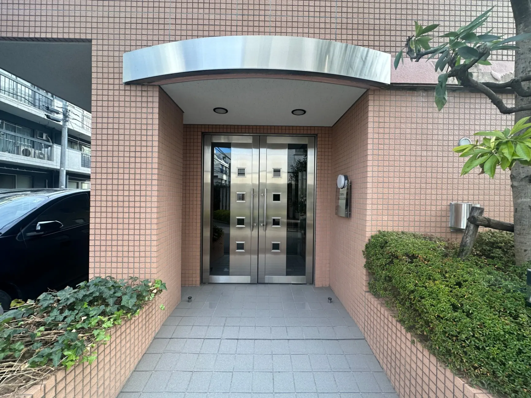 現代的な外観のマンションエントランス、ピンクのタイル壁、ステンレスの扉、クリアなガラス窓
