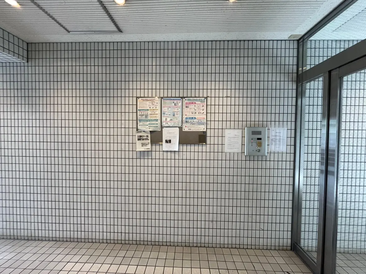 建物のエントランスホール、白いタイル壁、掲示板と自動ドア、清潔なデザイン