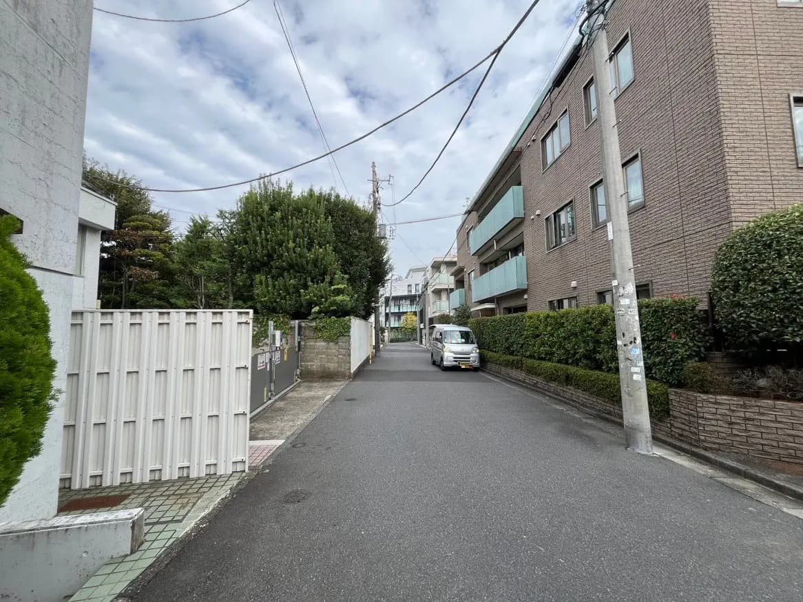静かな住宅街の通り、樹木とアパートが並ぶ風景、曇り空
