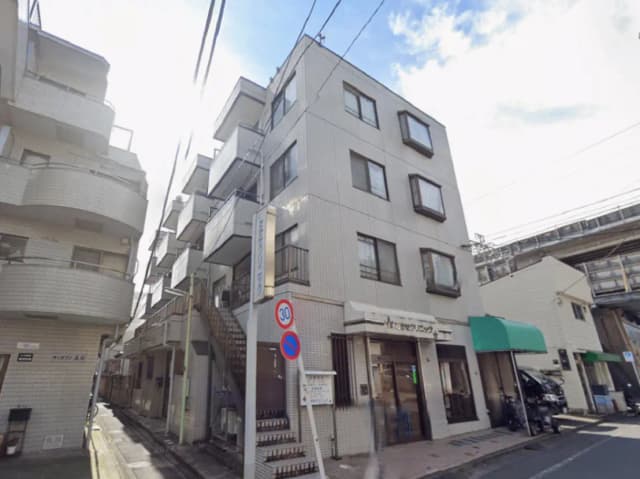 - 白い外壁とバルコニーが特徴のアパートメントビル、近くに自転車と看板が見える都市の風景