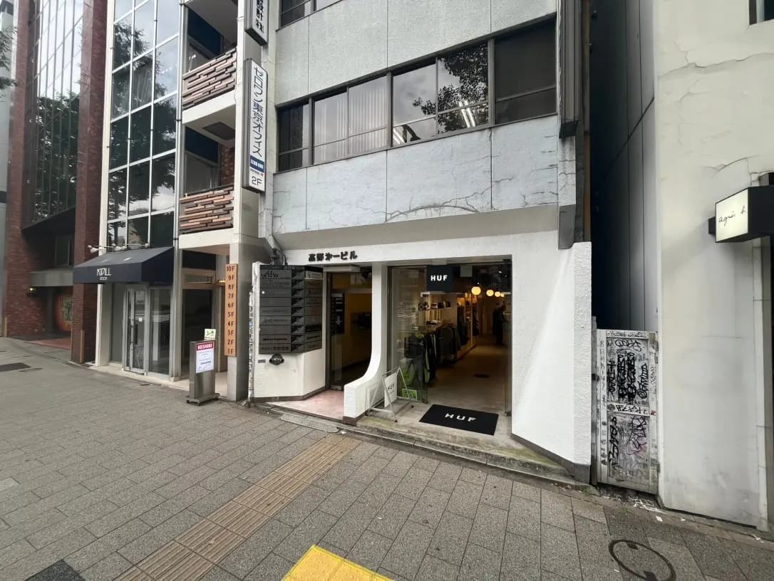 都会のオフィスビルの外観、入り口に案内看板、隣には衣料品店