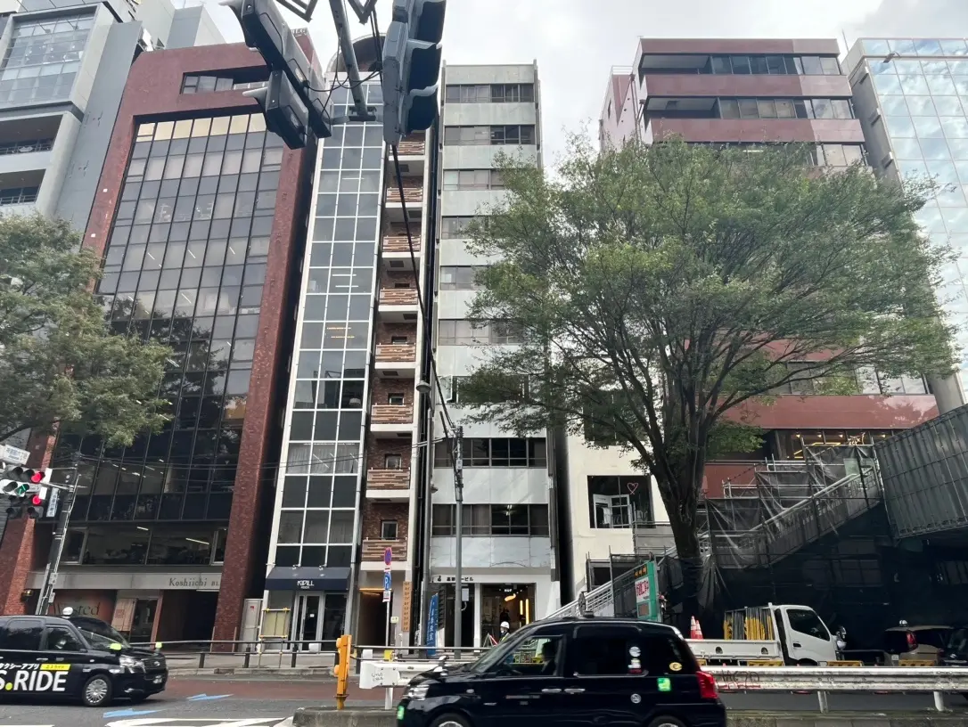 都会的な通りに面した現代建築のオフィスビル、大きな窓が特徴のファサード、緑豊かな木と街路樹