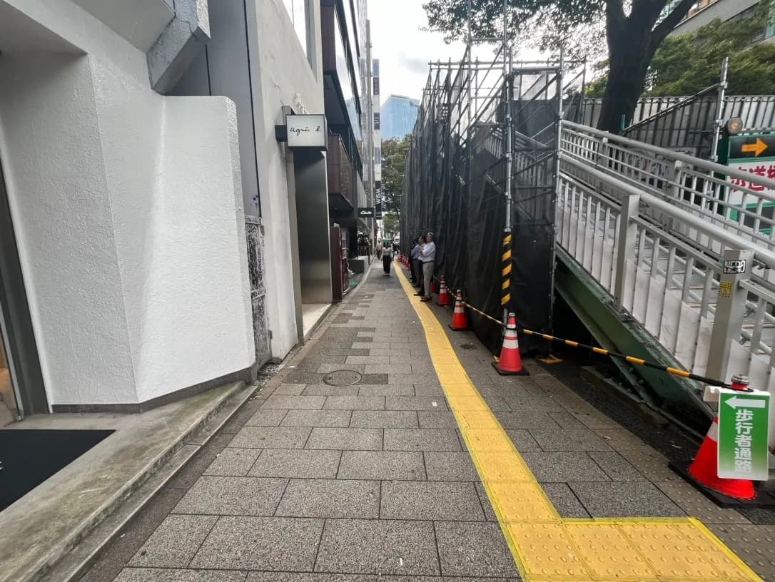 日本の都市部の歩道と工事現場、視覚障害者用の黄色い誘導ブロックと足場が覆われたビル