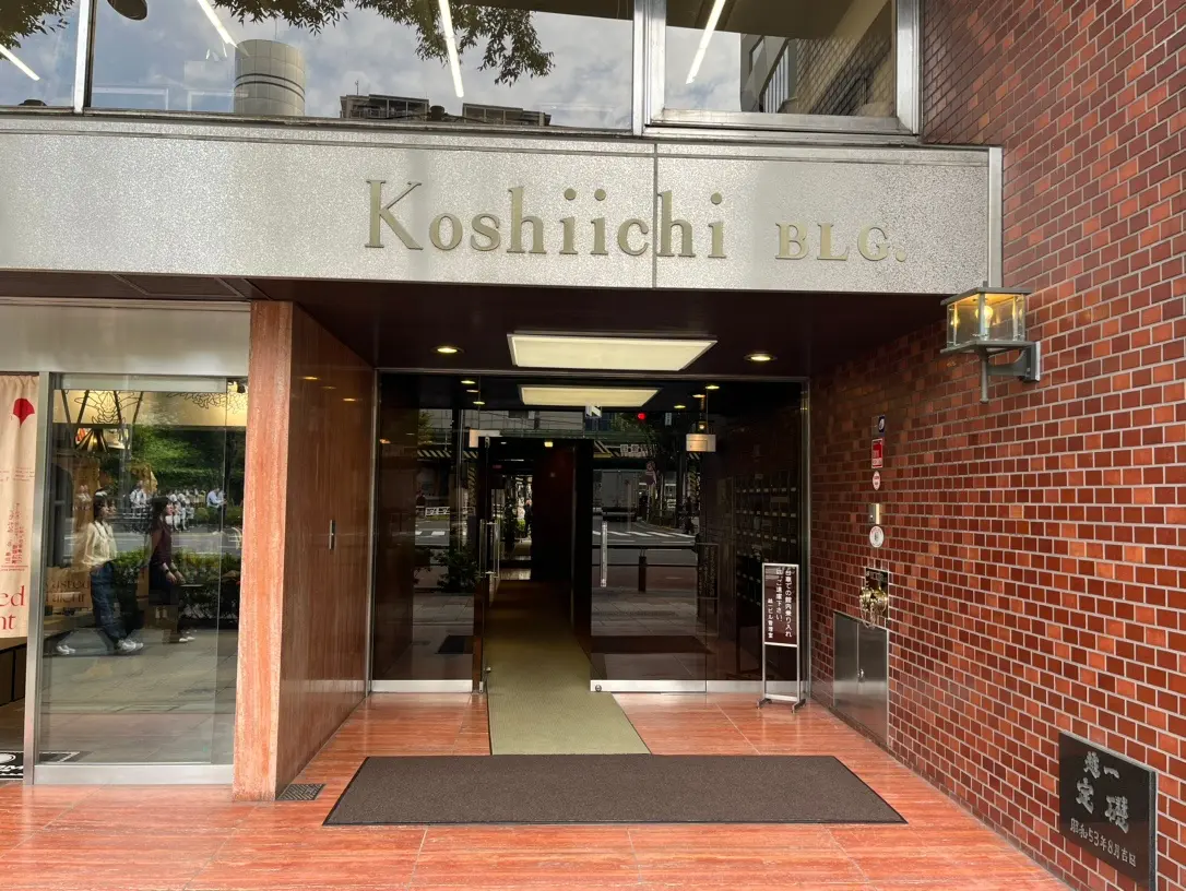 レンガ造りのビルのエントランス、看板に「Koshiichi BLDG.」の文字がある都市の建物