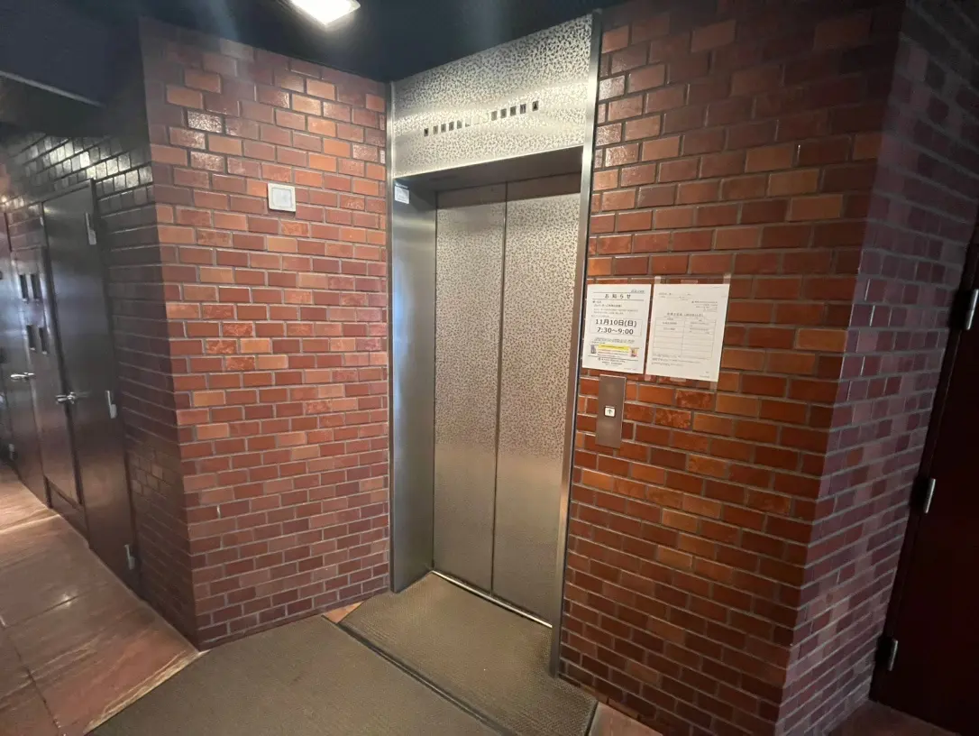 レンガ壁に囲まれたモダンなエレベーターの入り口、案内掲示板付き