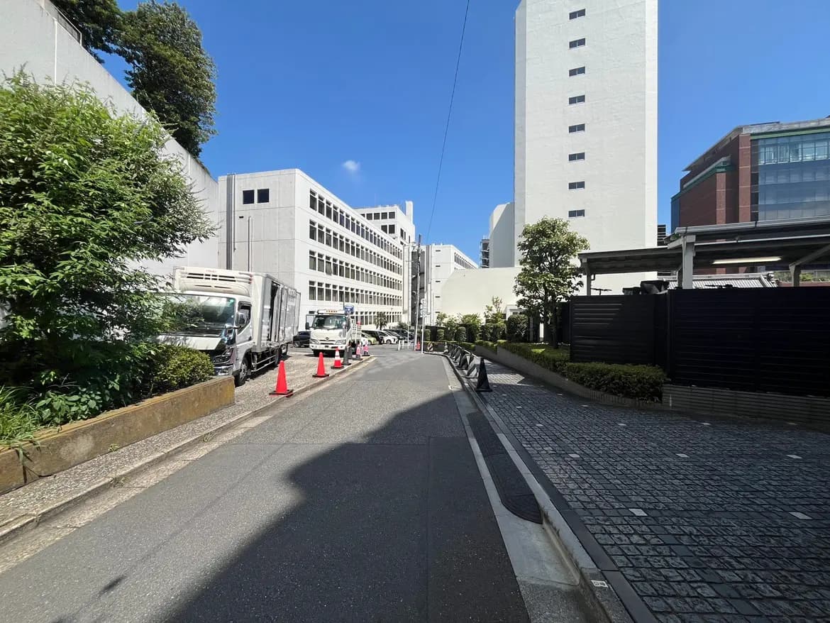 - 都市の道路風景、両側に高層ビルとトラックが並ぶ、青空と自然の緑が映えるシーン