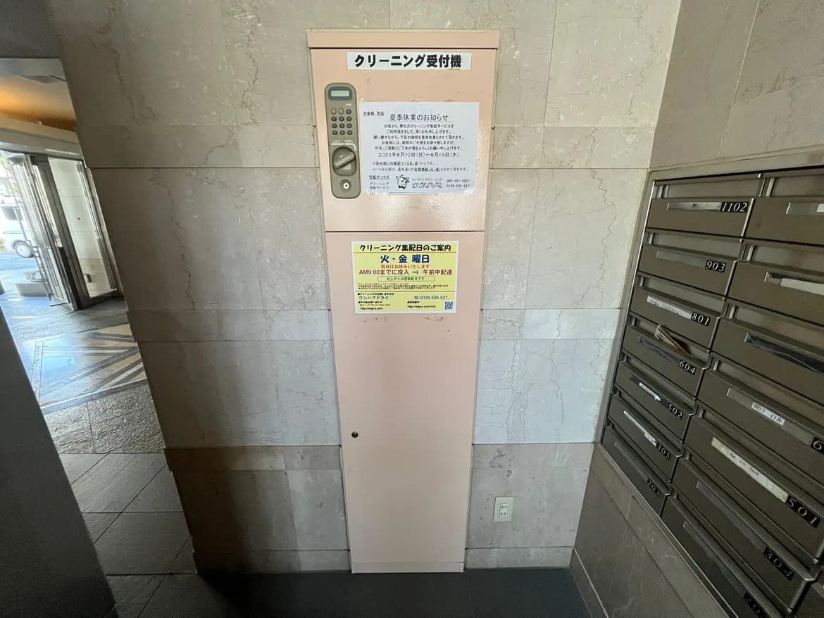 - クリーニング受付機の設置されたエントランスホール、隣に郵便受けが並ぶモダンな施設の内部状況