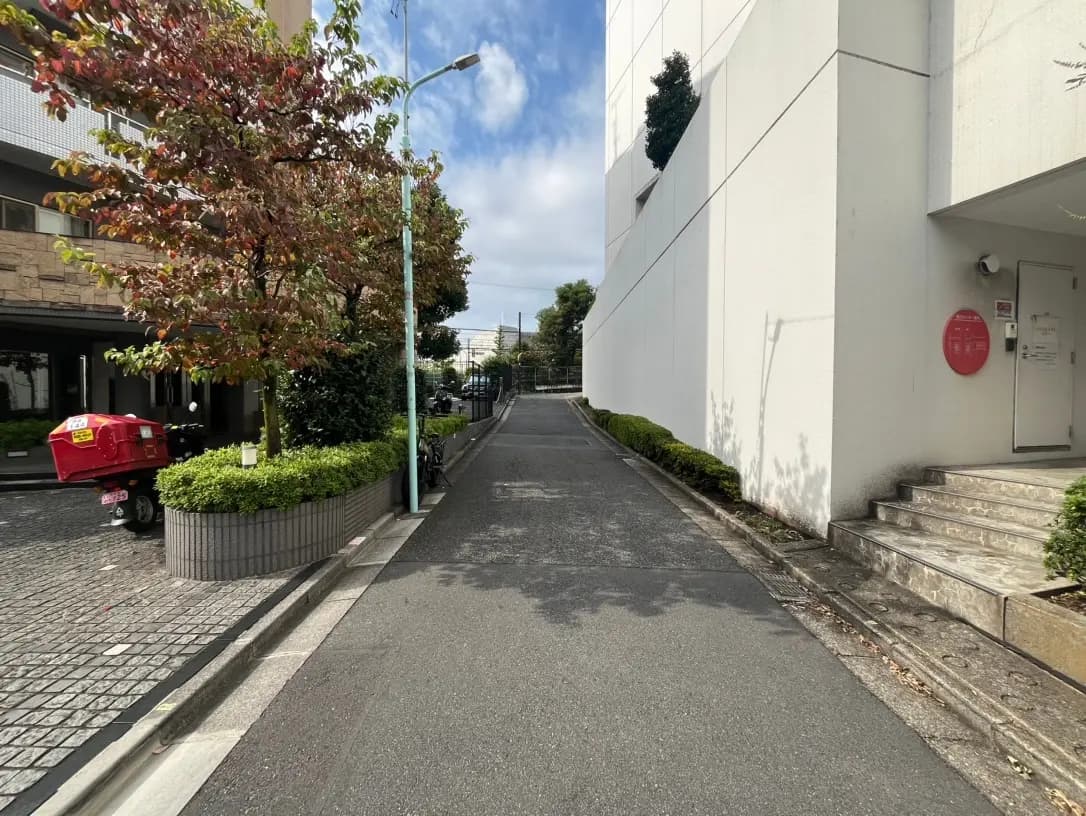 秋の季節感を感じる都市の歩道、紅葉する木々と配達用バイク、現代的な建物のエントランス