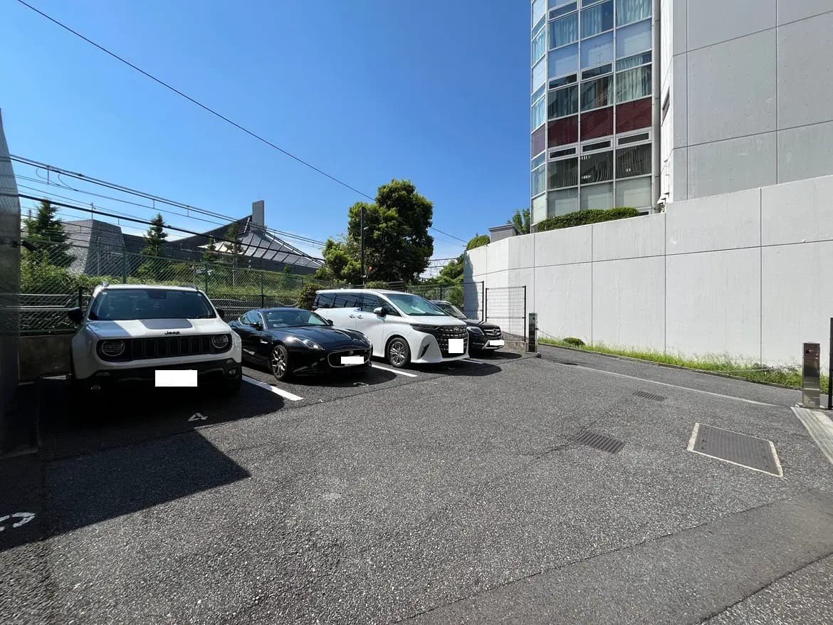 - 駐車場の風景、青空と近隣の建物、白と黒の自動車が並ぶ静かな環境