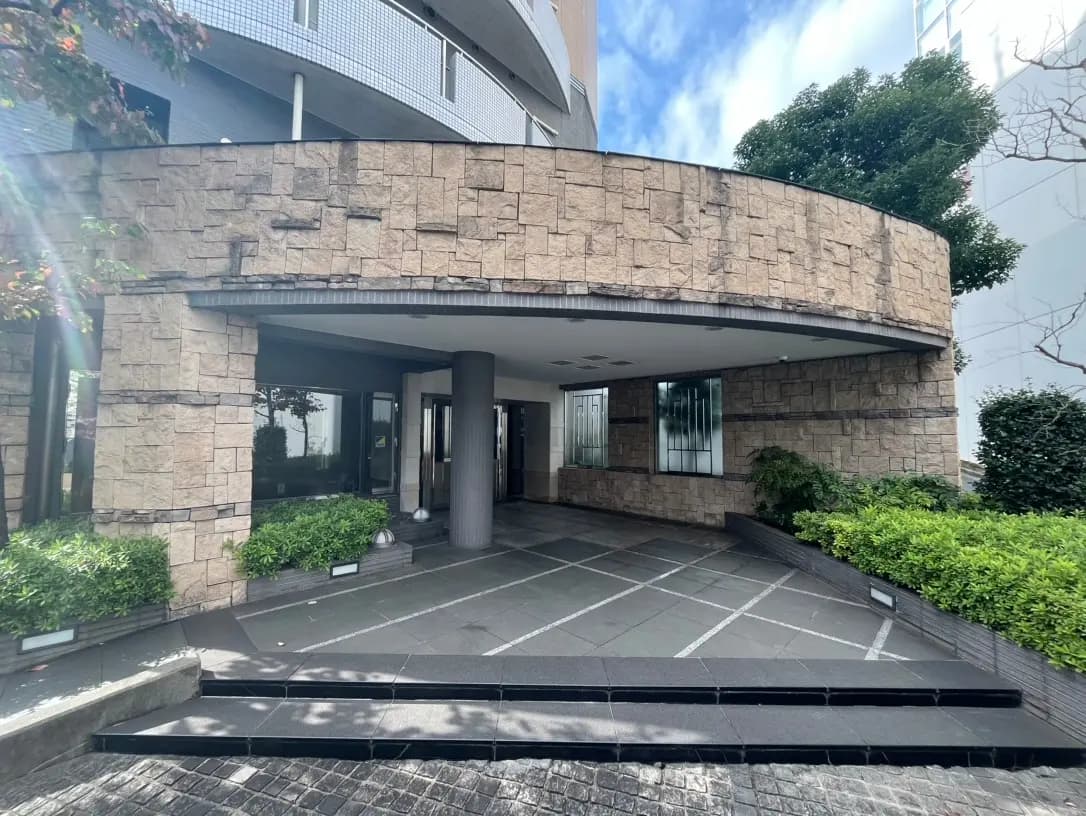 モダンな外観のマンションエントランス、石積みの壁とガラス窓、緑豊かな植栽