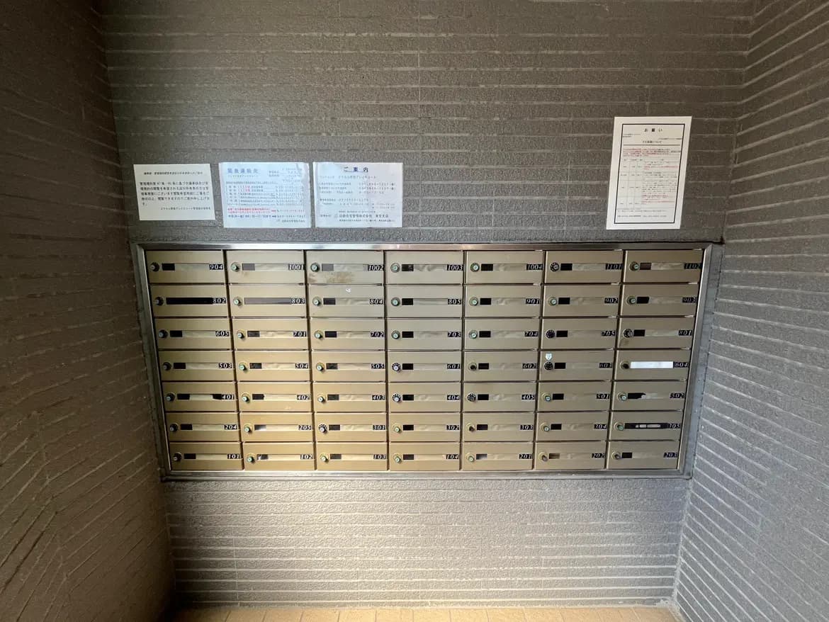 - 複数の郵便受けが並ぶエントランスの郵便ボックス、壁には利用案内の掲示がある内部の様子