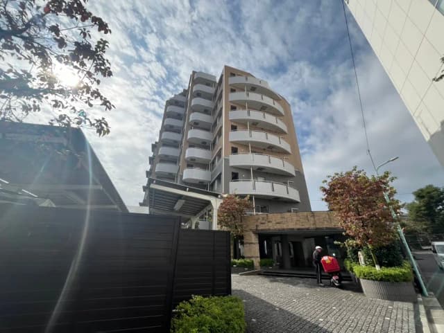 晴れた日の街並みとモダンなマンション、エントランスには配達員と赤い配達カート