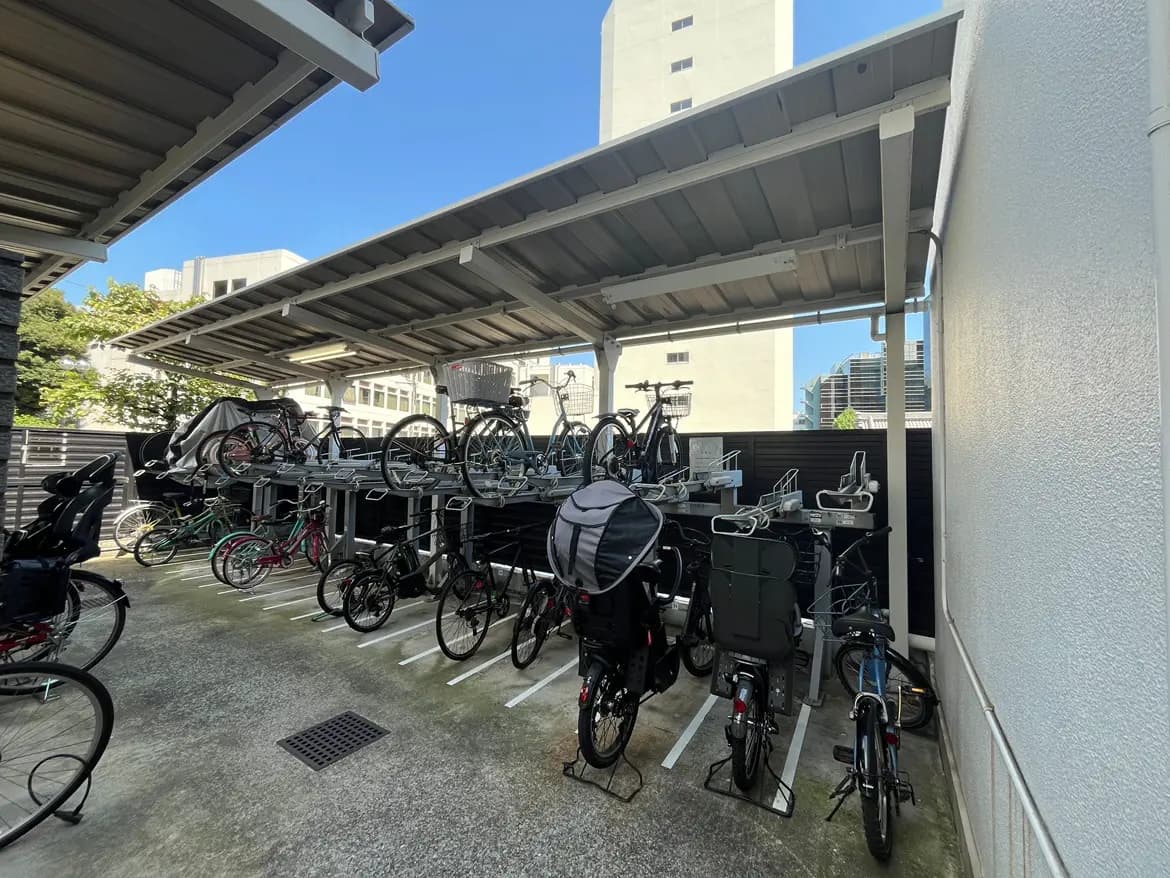 - 自転車駐輪場の風景、屋根付きの駐輪スタンドに並ぶ様々な自転車と明るい青空