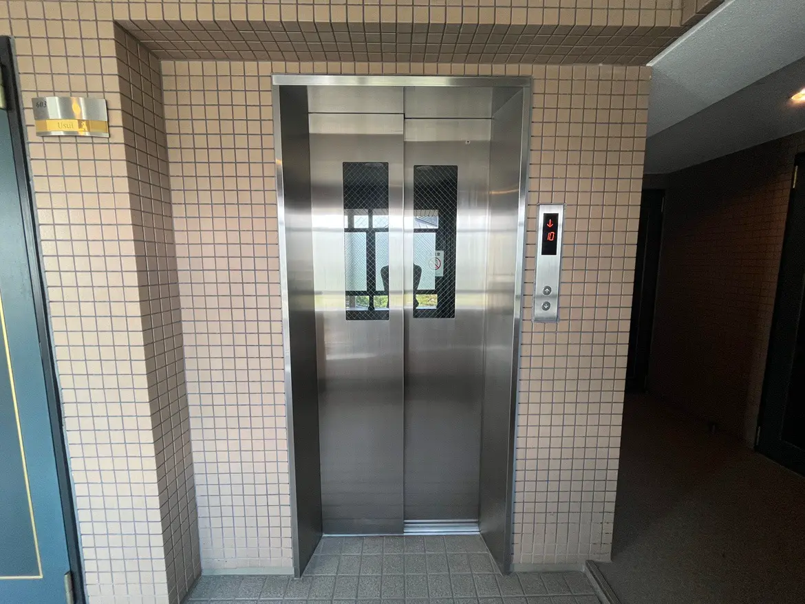 - モダンなデザインのエレベーターが設置されたマンションのロビー、タイル張りの壁とボタンパネルを特徴とする空間