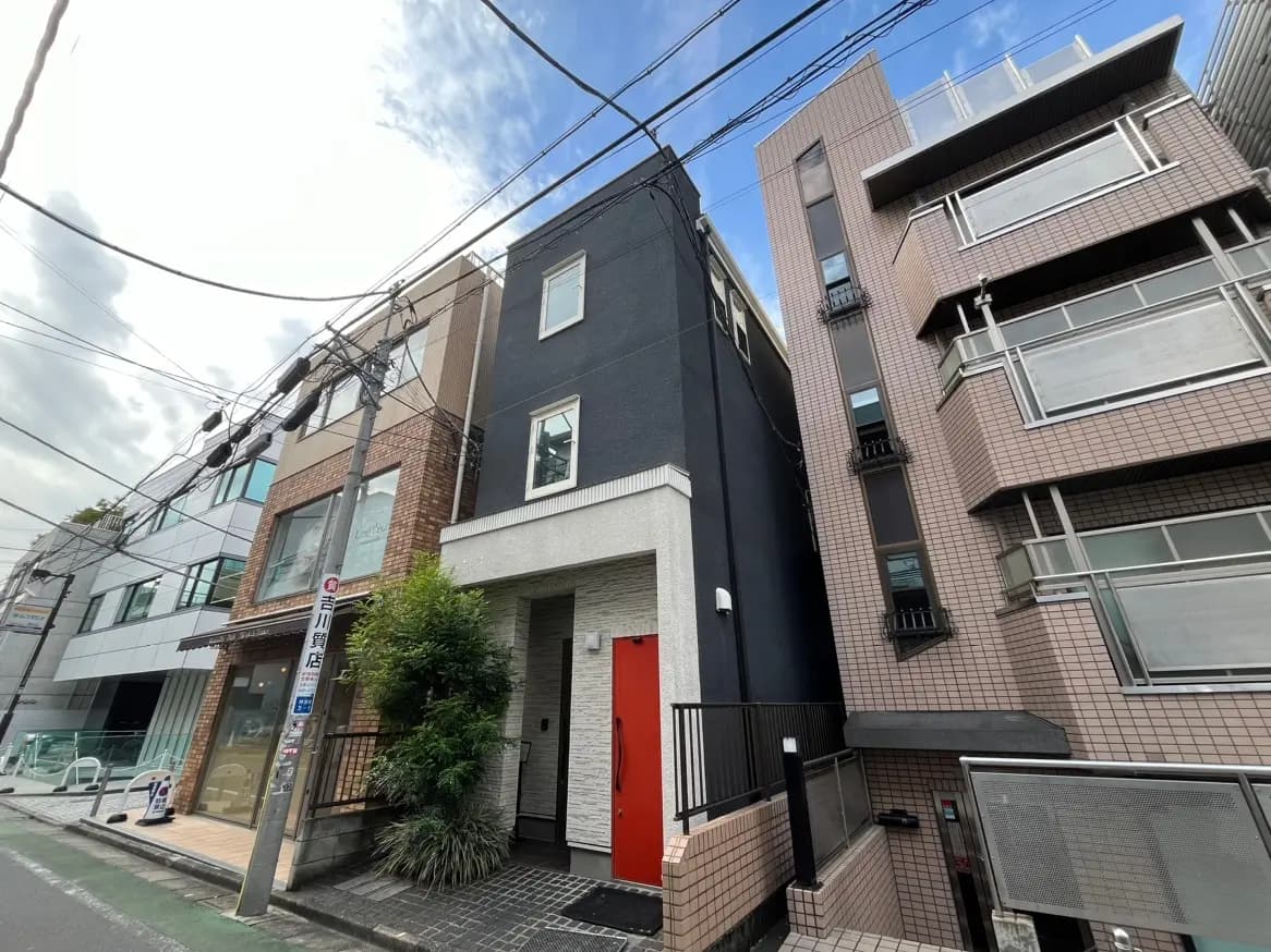 都市の環境に溶け込むモダンなデザインのアパート建物、黒と白の外壁、赤いドアが特徴