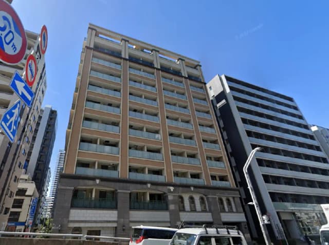 - 高層マンションの外観、バルコニー付きのデザイン、周囲のビルや交通標識が見える都市風景