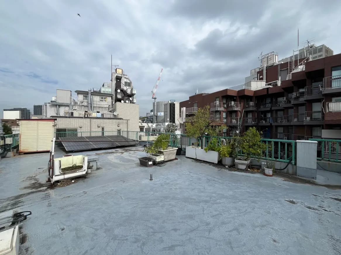 日本の都市部の屋上からの眺め、プランターに植えられた緑の植物、建物の屋外機器、遠くにクレーンが見える光景