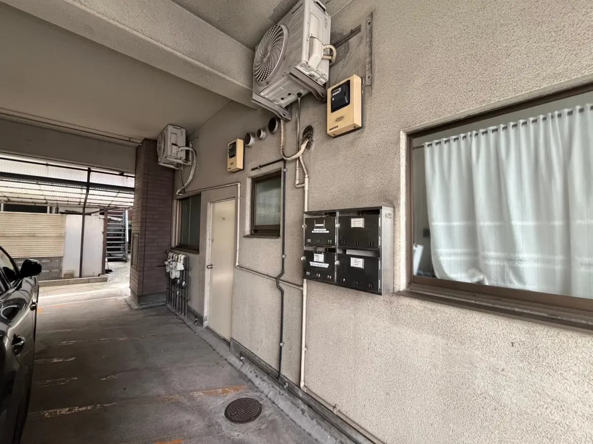 マンションのエントランス近くの壁面、配管とエアコン室外機、郵便受けと窓、日常の住宅シーン