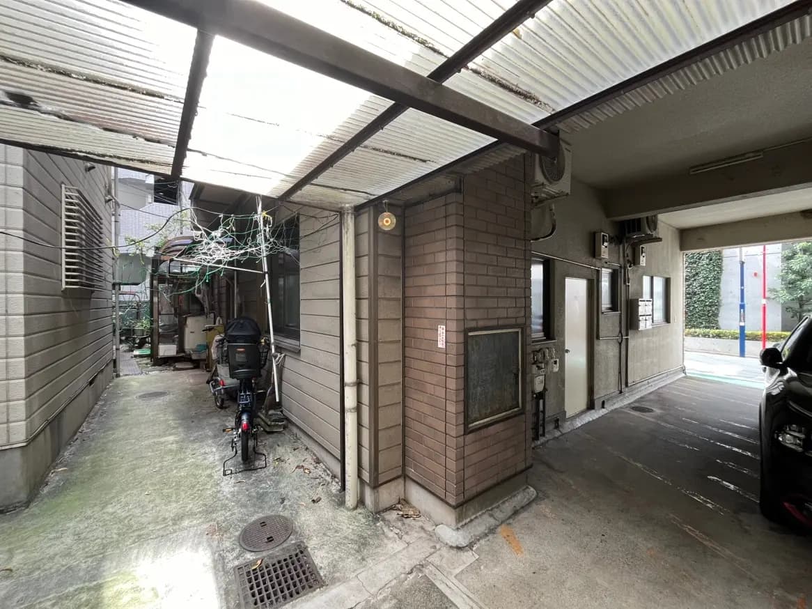 建物の外側にある屋根付き駐車場、バイク駐輪スペース、通路に生い茂る植物