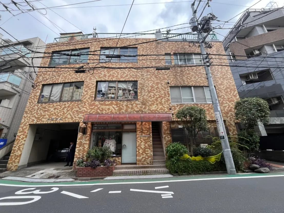 都市の路面に面したレンガ造りのビル、一階には小さな店舗があり駐車スペースつき