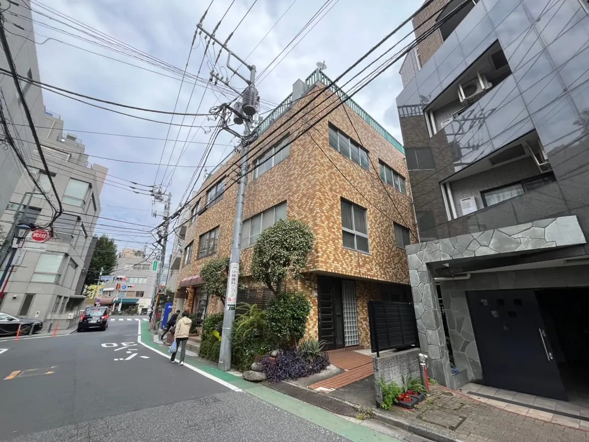 都市の通りにあるレンガ造りのモダンな建物、周囲には他の建物や電柱、歩行者が見える風景