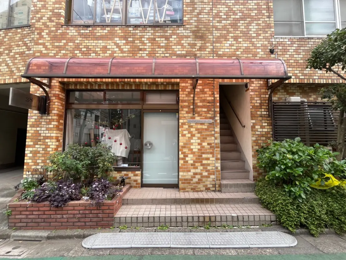 都市の煉瓦造りのビルの入り口、植物が置かれた歩道、店舗のガラス扉