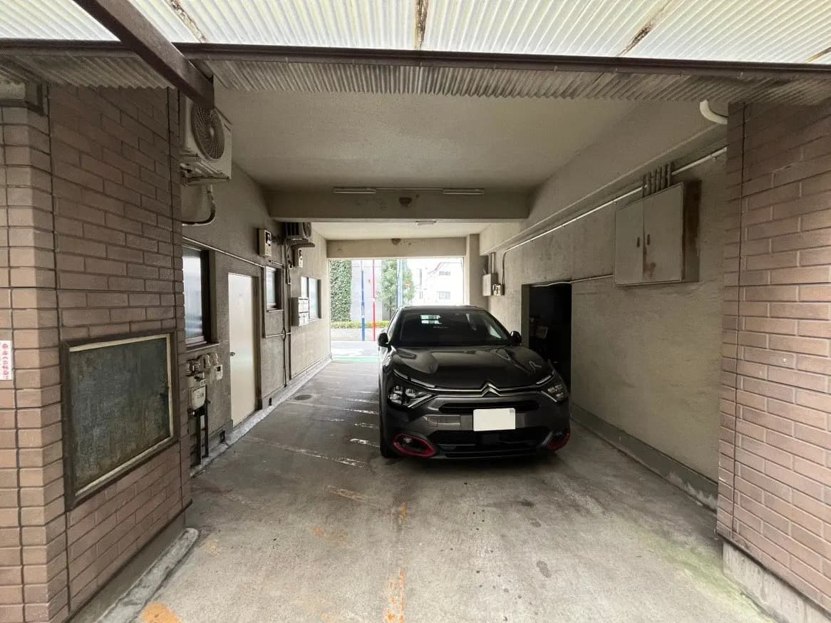 都市のアパートの駐車スペースに停められた黒いセダン車、レンガ造りの建物と屋根付きのエントランス