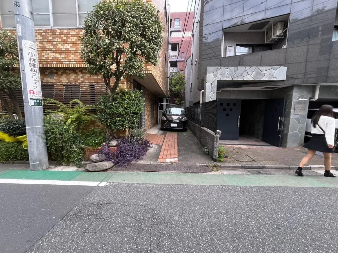 日本の都市部にある住宅街の通り、歩行者と駐車中の車、緑豊かな植栽が見える風景