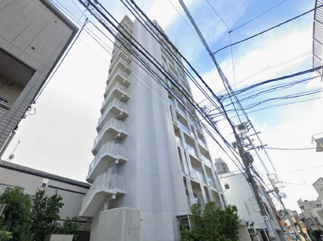 - 白を基調としたモダンなマンション、バルコニーと窓が特徴的で、周囲には電線が張り巡らされた都市の風景