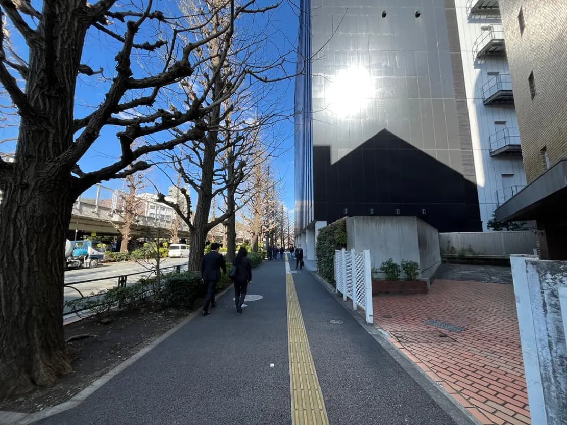 - 青空の下、並木道を歩く人々と近代的なビルの反射、周囲の植物と街並みの風景