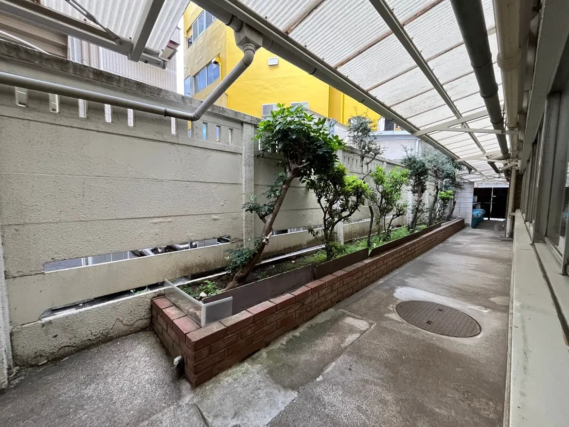 - 薄暗い通路、緑の植栽とレンガの花壇、雨よけの屋根がある静かなスペース