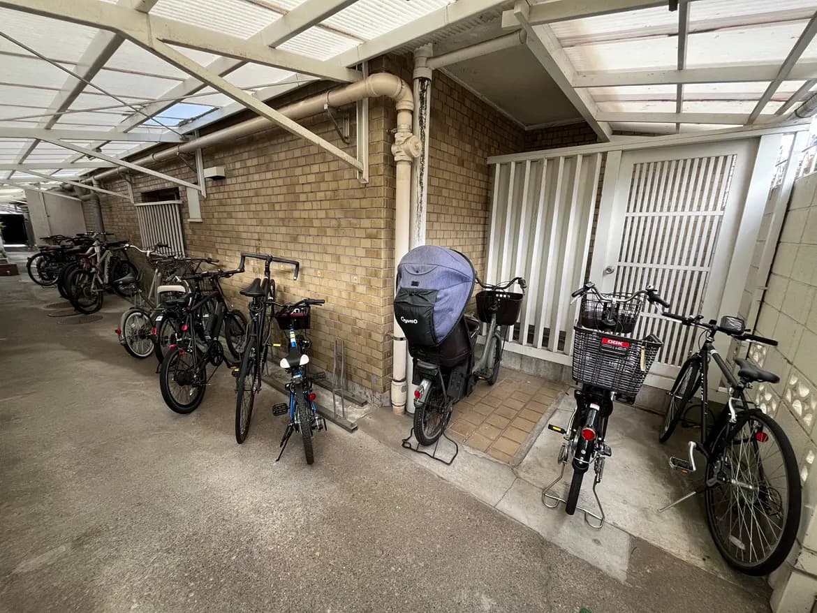 - 自転車置き場に並ぶ複数の自転車、レンガ造りの壁と屋根がある屋内スペースで整然とした配置