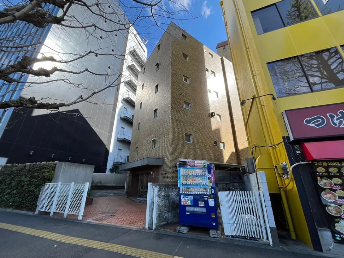 - 都市の風景にあるレンガ造りの建物と隣接する高層ビル、ビビッドな黄色の店舗と自販機が映える通りの様子