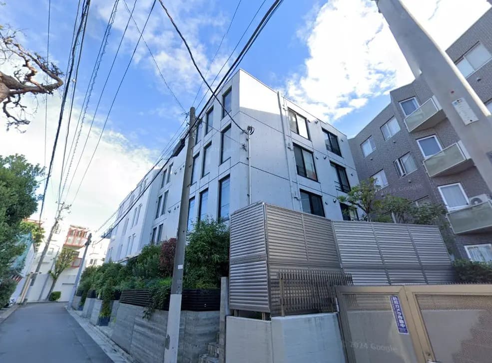 現代的な外観の住宅街のアパートメントビル、青空と電線、歩道に面した通り