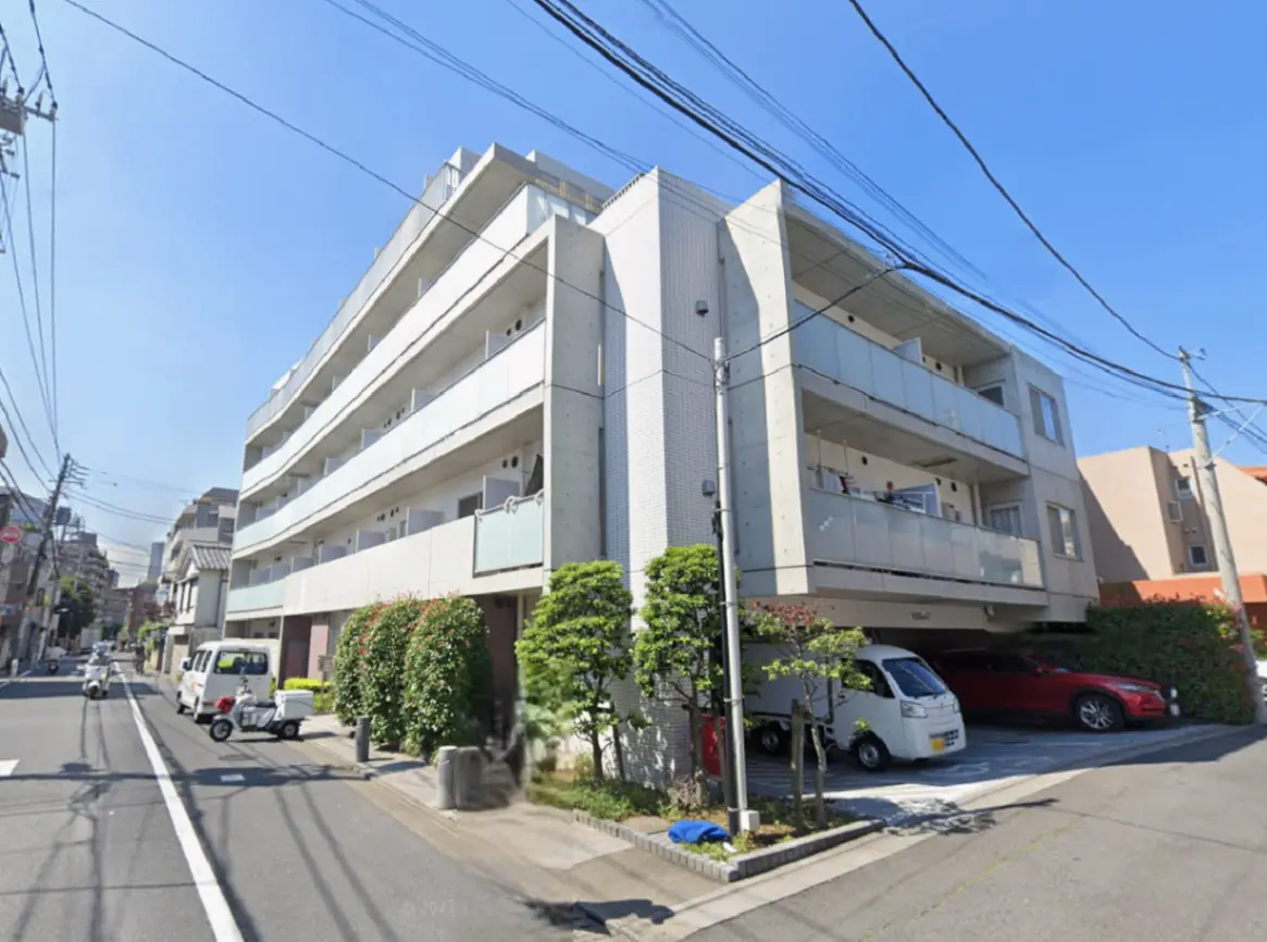 - 現代的なデザインのマンション外観、青空を背景にした四階建ての建物、周囲に植栽や車が駐車している様子