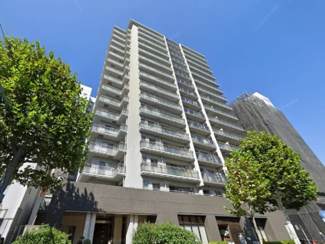 - 現代的なデザインの高層マンション外観、青空の下に立つ、周囲には緑の樹木と草花が見える景観