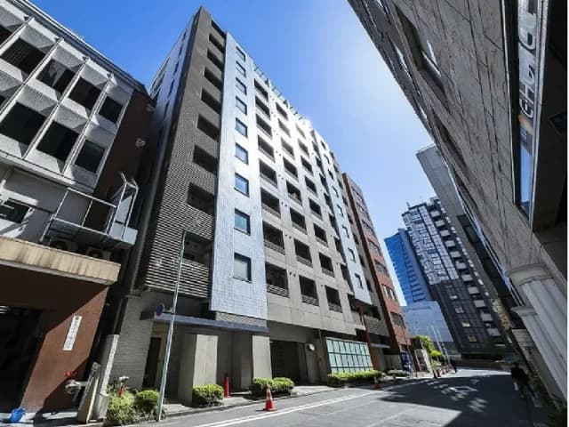 - 都市のビル群の中に立つモダンな外観の高層ビル、青空を背景にした街並み