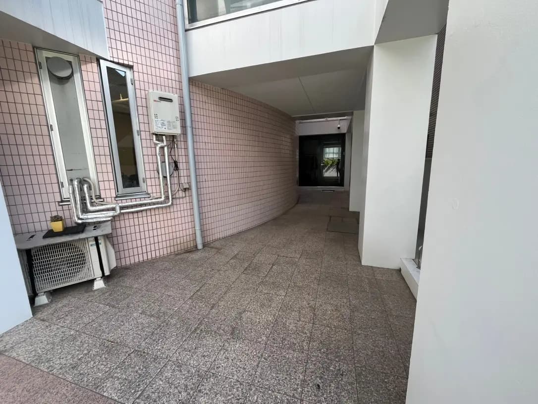 現代的な建物のエントランス、ピンクタイルの壁、室外機と排水管が見える