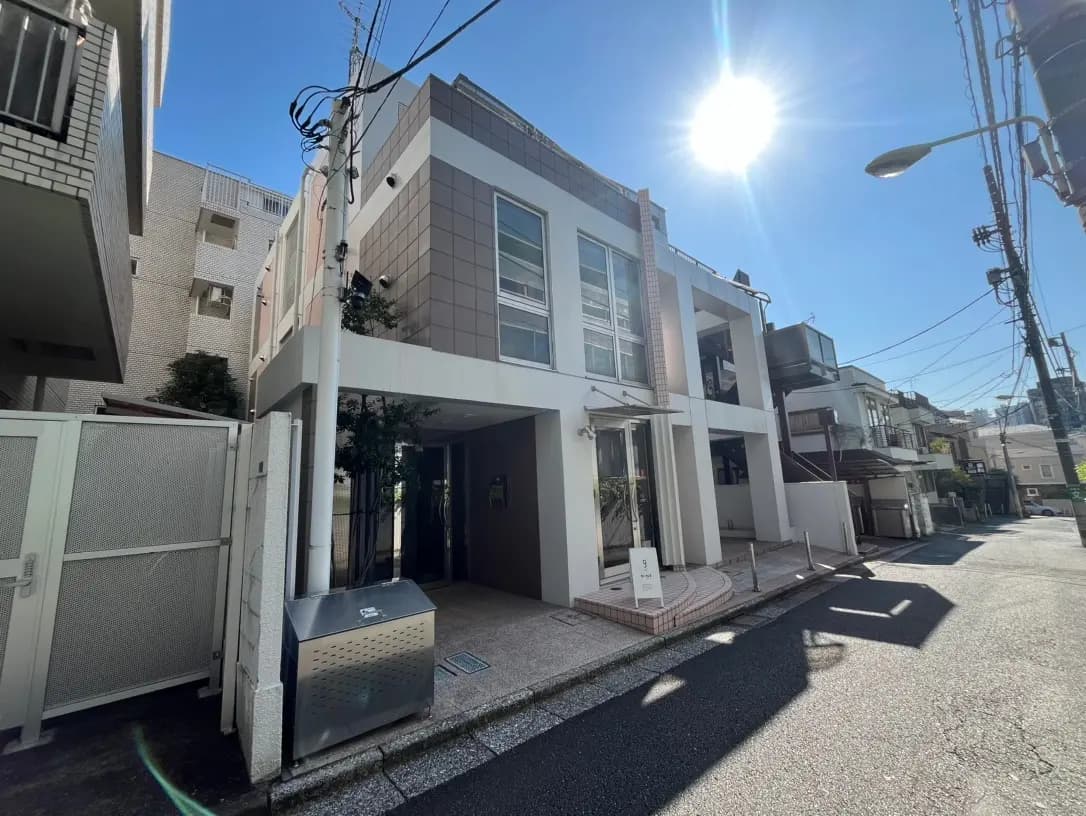 日差しが強い晴れた日に撮影された都市のアパート外観、現代的な建築スタイル、歩道と街路灯が見える